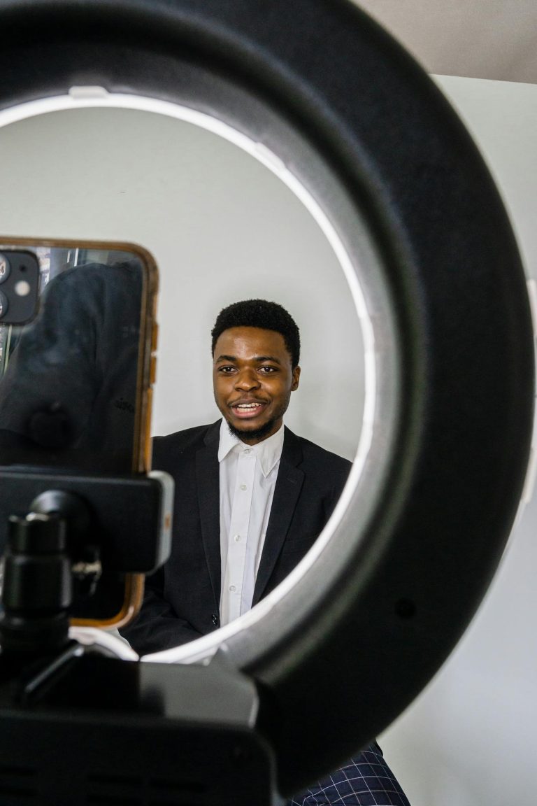 A professional adult using a smartphone and ring light setup for filming indoors.