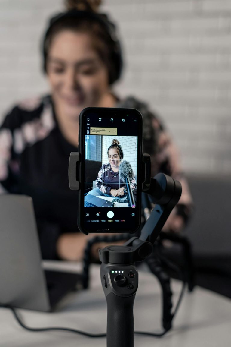 A woman using a smartphone on a tripod to record content indoors.