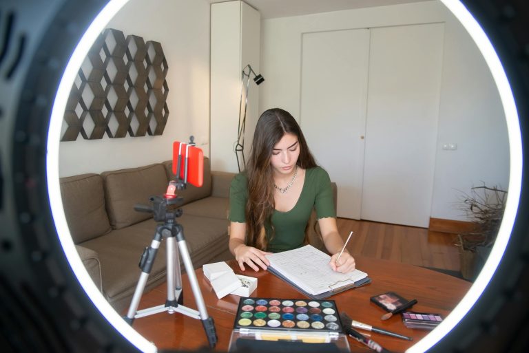 A young woman writing notes and creating video content at her desk with a ring light.